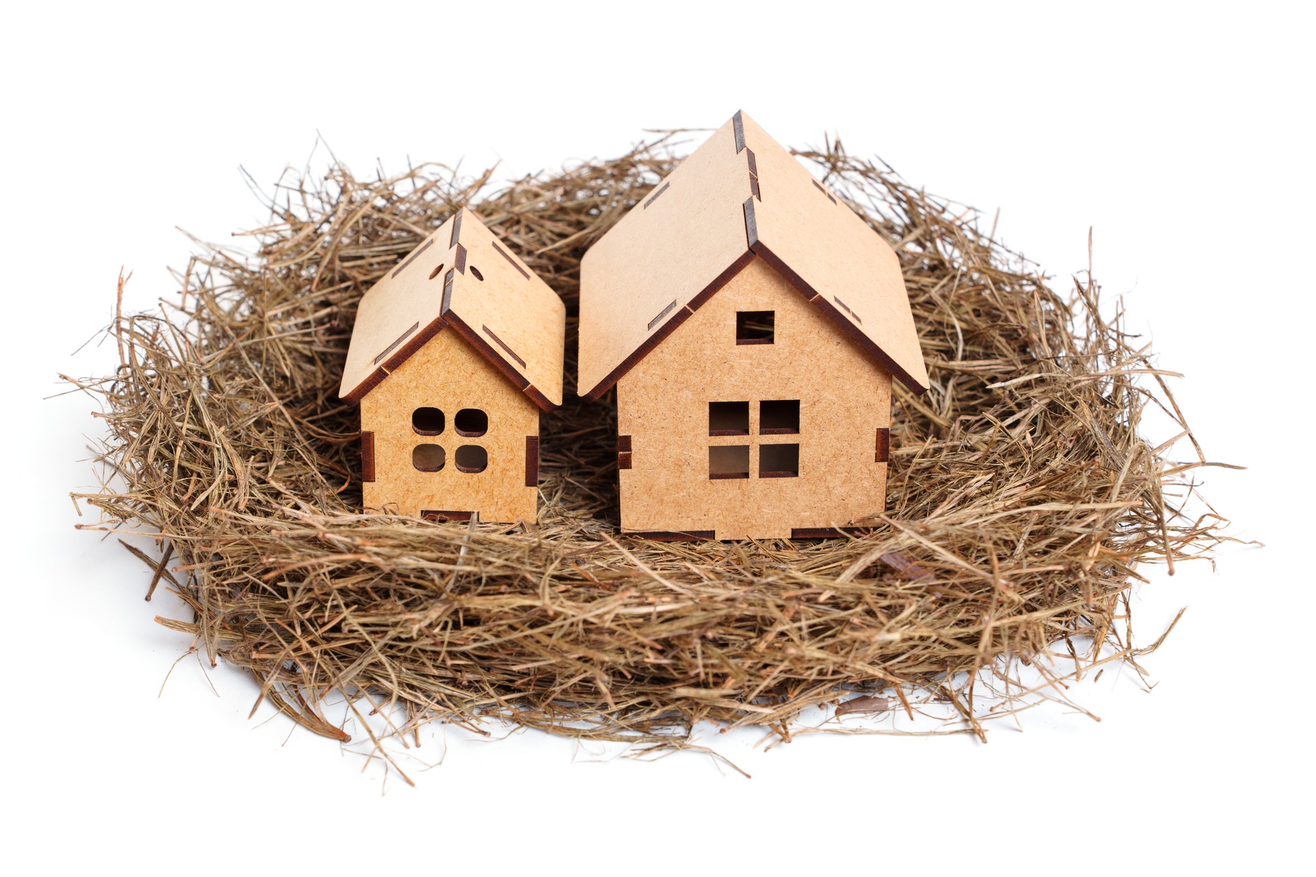 Bird's nest with two toy wooden houses on gray