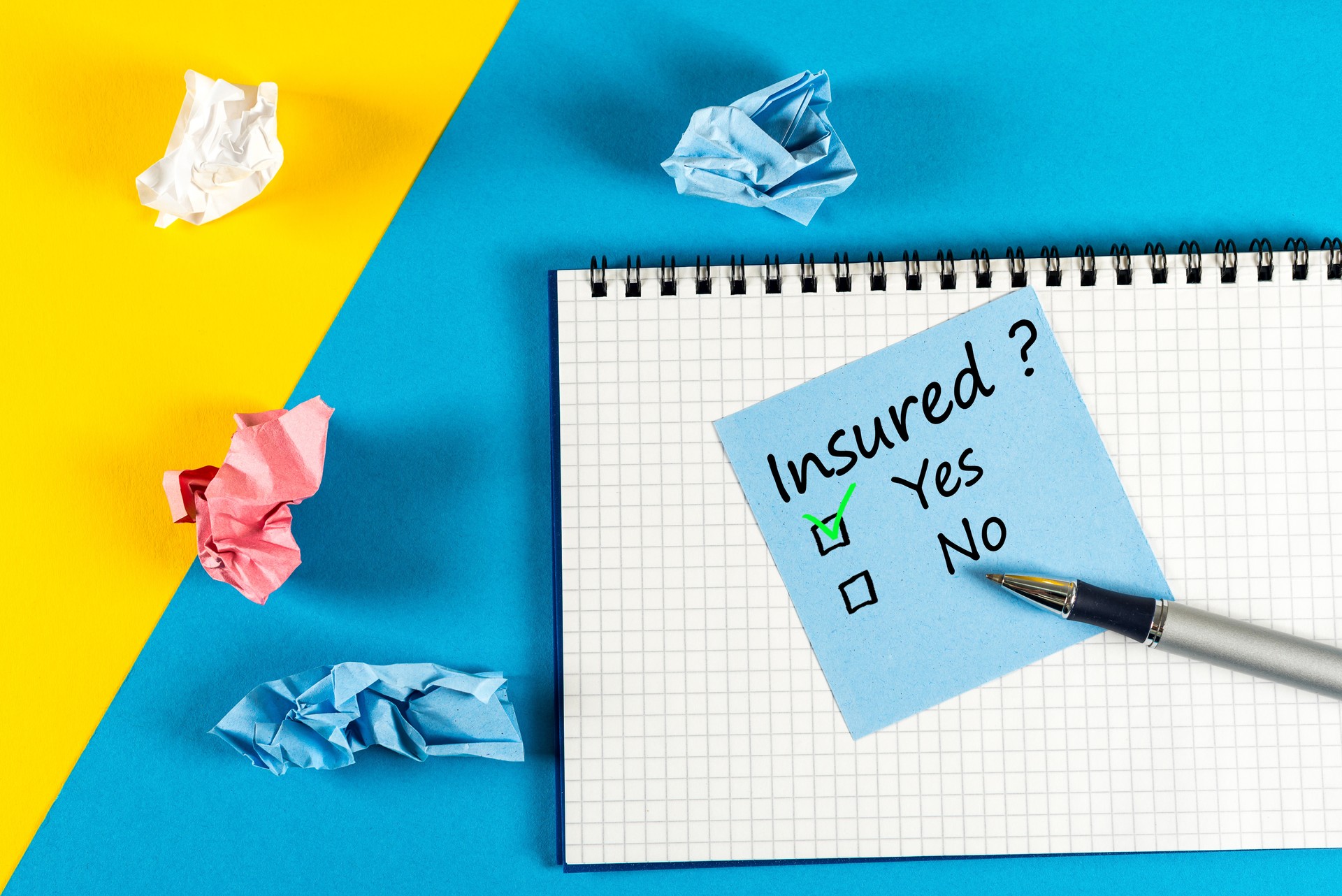 Survey with question Insured, Yes or no. Message at notepad at yellow and blue table, insurance agent